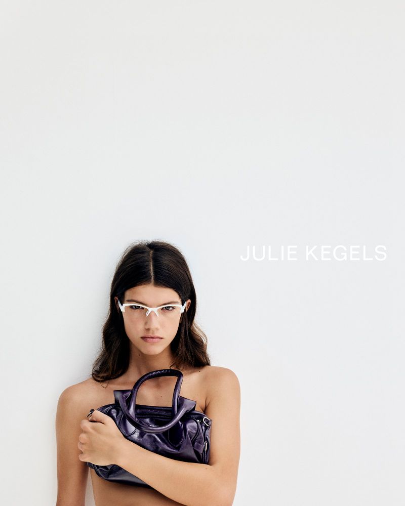 Model wearing white sunglasses holding a glossy purple leather handbag against a white background