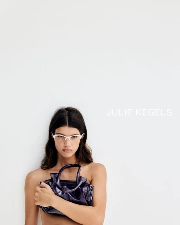 Model wearing white sunglasses holding a glossy purple leather handbag against a white background