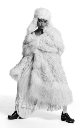 Sophie Wilde wearing a voluminous white faux fur coat and matching fluffy hat against a plain background