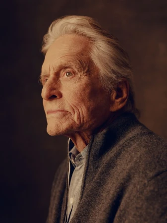 Portrait of Michael Douglas looking to the side in a dark jacket against a textured dark background