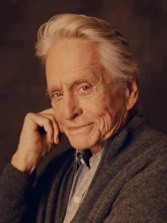 Portrait of Michael Douglas with white hair and grey cardigan against a dark textured background