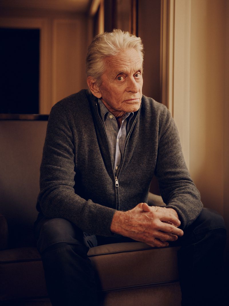 Portrait of Michael Douglas seated in a chair wearing a grey zip-up sweater for LA Times by photographer David Urbanke.