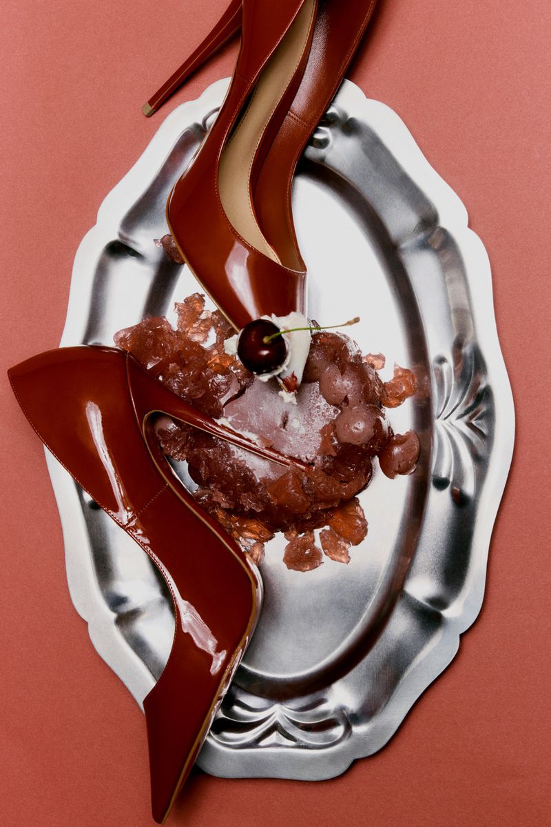 Glossy red patent leather high heels arranged on a silver platter with a dessert topped with a cherry