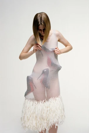 Model wearing a sheer dress with stiletto shoes pressing through the fabric against a white seamless background