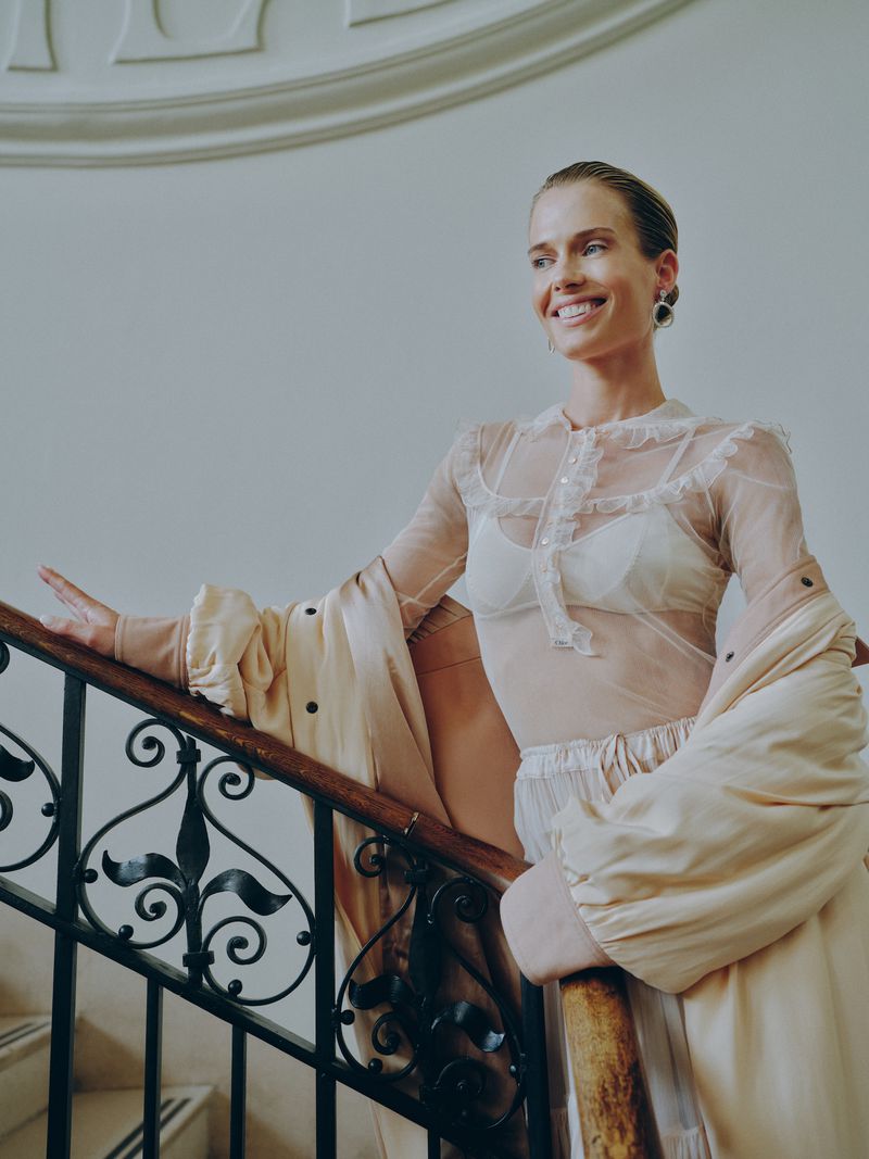 Lady Amelia Spencer on stairs wearing a sheer ruffled blouse and a coat draped over her shoulders