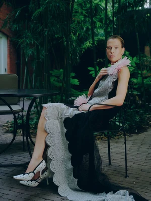 Woman in a black and white dress with pink feather accents seated on an outdoor patio chair