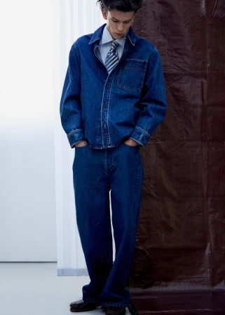 Young man standing in dark blue denim shirt and jeans with striped tie, shot for M Le magazine du Monde.