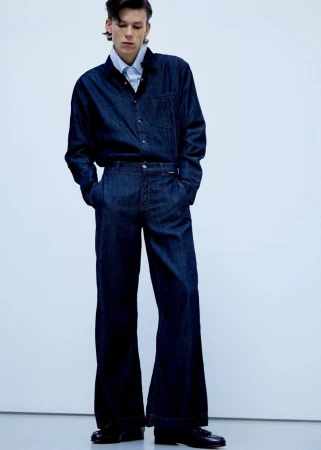 Model standing in dark denim shirt and matching trousers against a pale studio background for editorial project Le grand bleu.