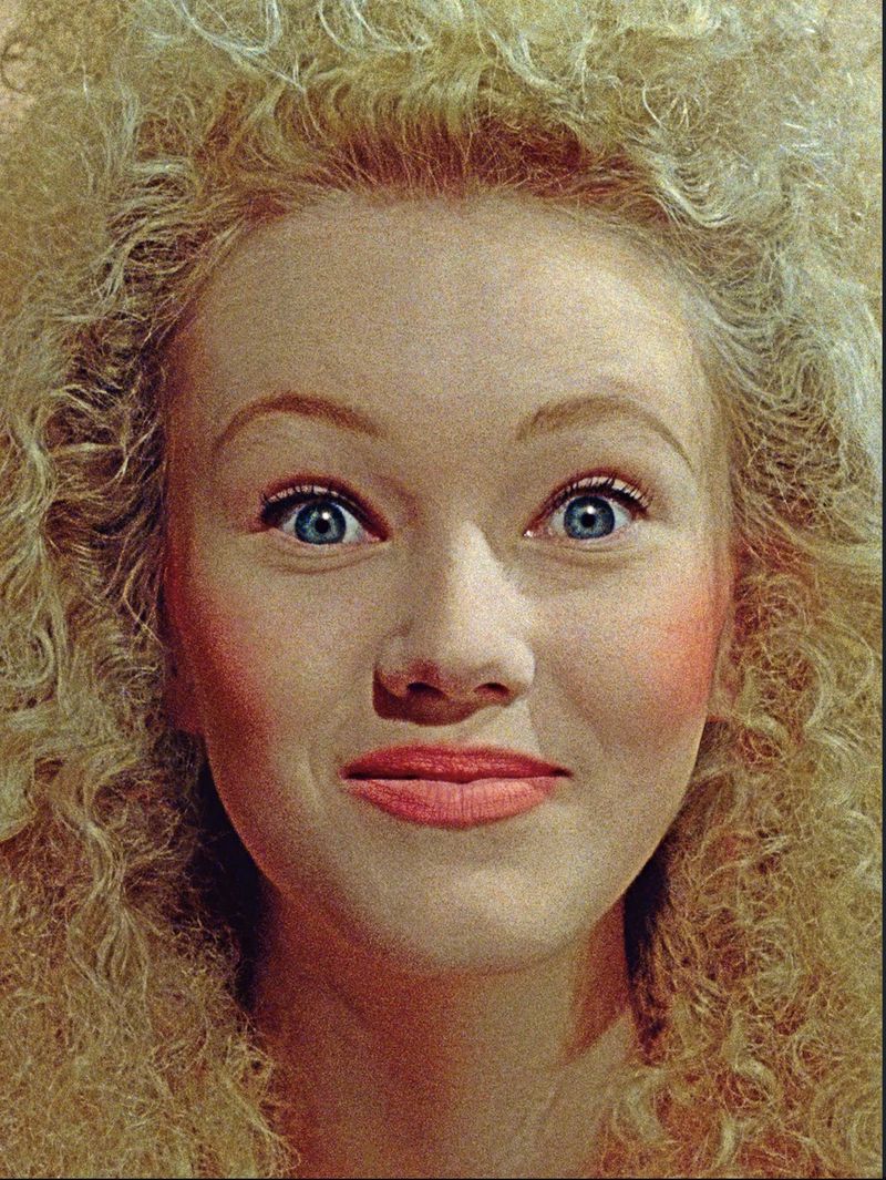 Close-up portrait of a woman with voluminous blonde curly hair, blue eyes, and pink blush for D Repubblica New Wave editorial