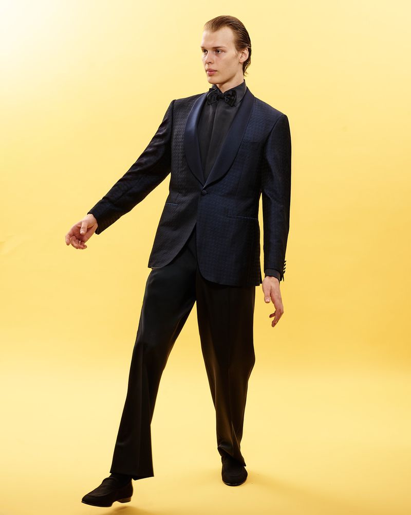 Man wearing a dark patterned tuxedo suit and bow tie against a solid yellow background for Canali