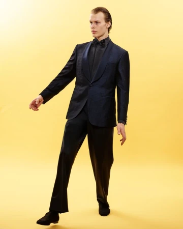 Man wearing a dark patterned tuxedo suit and bow tie against a solid yellow background for Canali