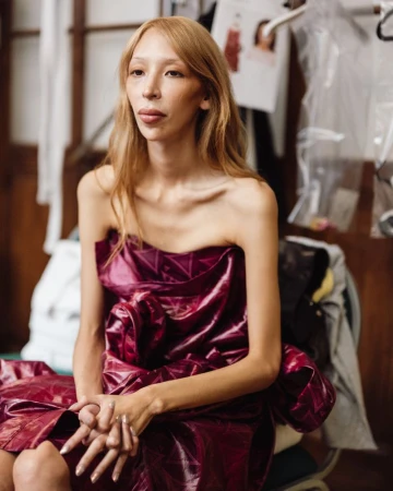 Model wearing a glossy plum strapless dress seated backstage during Vivienne Westwood fashion collection