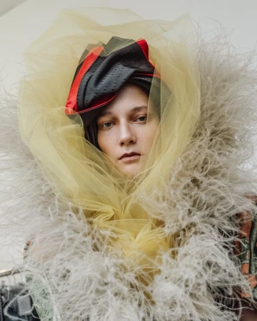 Model wearing feathered collar and yellow tulle headpiece backstage at Vivienne Westwood S/S 27