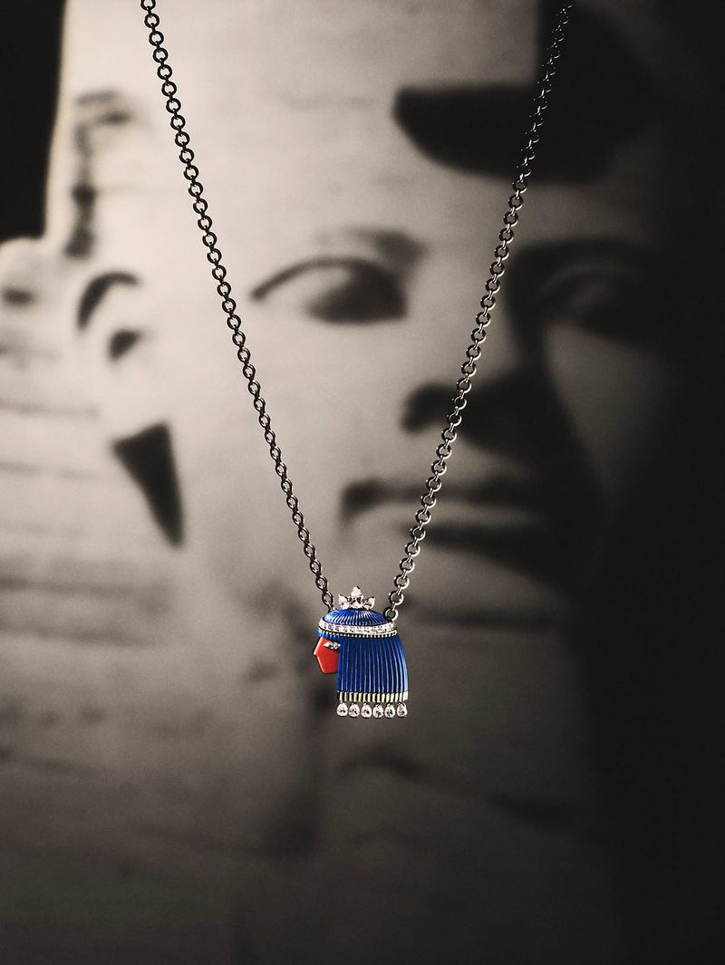 Close-up jewellery product shot of a silver chain necklace with a pharaoh pendant featuring blue and red enamel against a dark background