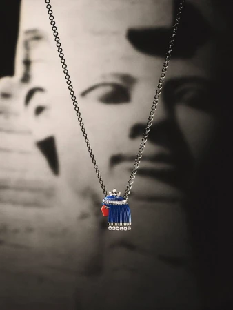 Close-up jewellery product shot of a silver chain necklace with a pharaoh pendant featuring blue and red enamel against a dark background