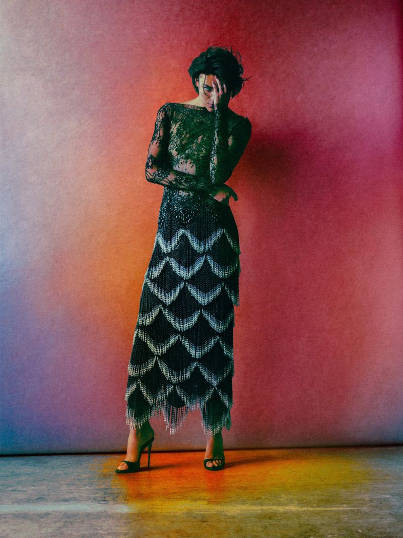 Model in black beaded lace dress with fringe standing against vibrant gradient background by Ryan Tandya