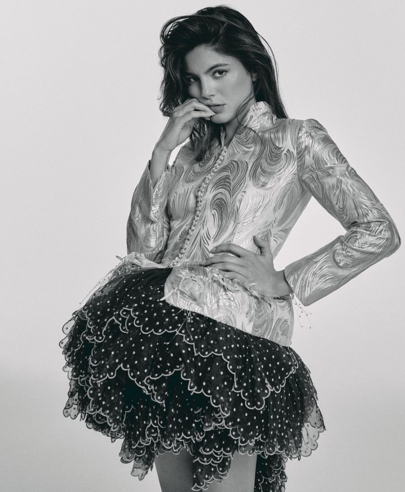 Monica Barbaro in a patterned patterned metallic top and ruffled polka-dot skirt against a light background
