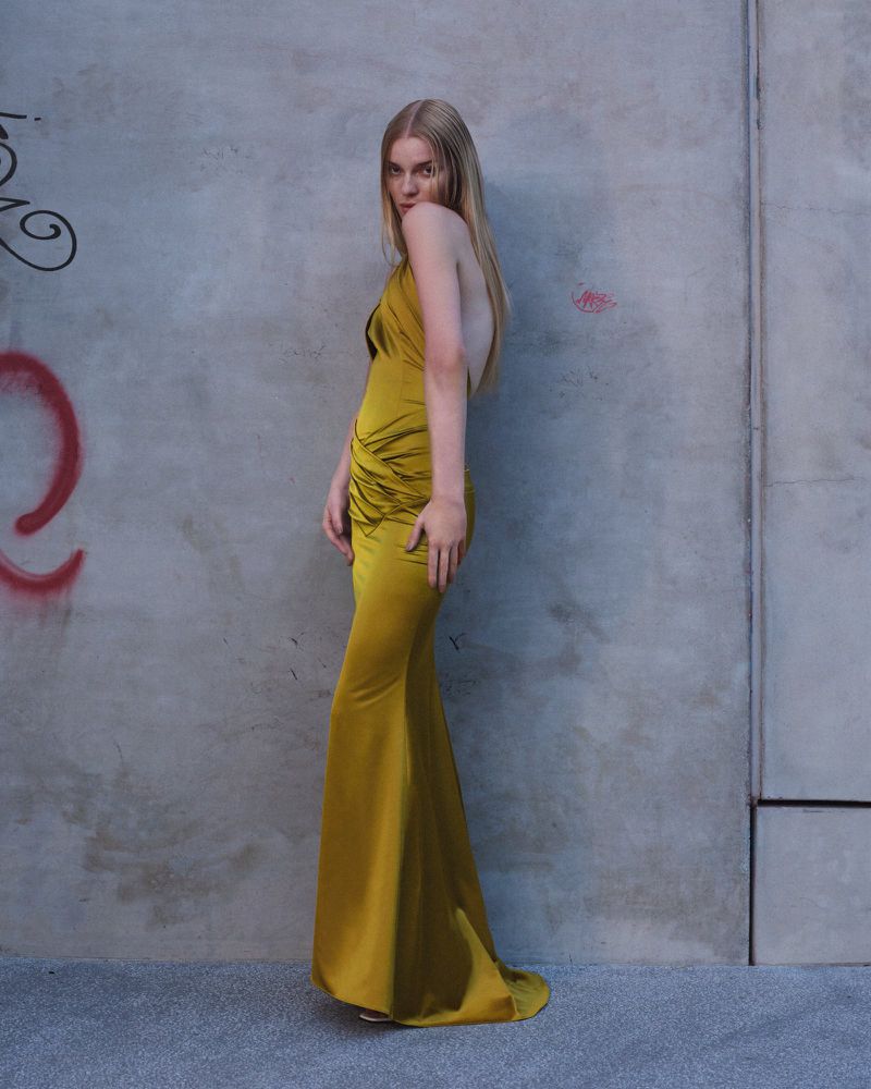 Model in a long gold satin gown standing against a concrete wall with graffiti for Giuseppe di Morabito lookbook