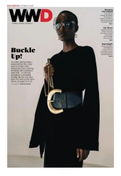 Model wearing a black top, statement belt, and visor sunglasses against a white seamless background for WWD.