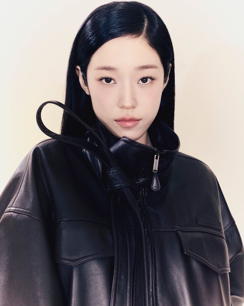 Close-up portrait of a young woman with long black hair wearing a black leather jacket against a light backdrop