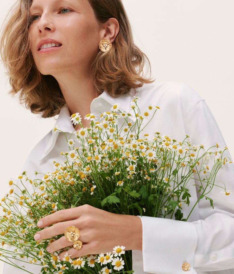 Model in white shirt holding a bouquet of small white flowers wearing gold jewelry for Vever Jewelry
