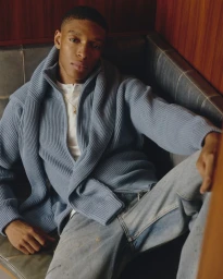 Black man seated in a booth wearing a blue zip-up sweater and jeans for FIVEFOURFIVE FW26