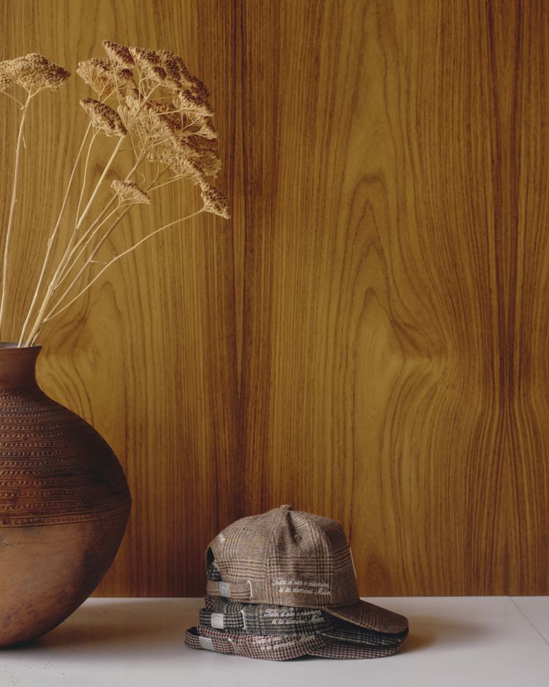 Stack of plaid caps and ceramic vase with dried flowers against wood paneling and white surface