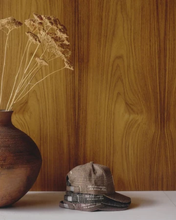 Stack of plaid caps and ceramic vase with dried flowers against wood paneling and white surface