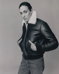 Portrait of Imane Khelif wearing a black leather jacket with a white shearling collar and denim jeans against a plain neutral background.