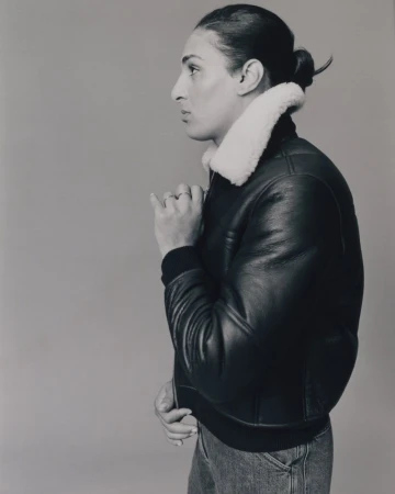 Portrait profile of Imane Khelif wearing a black leather jacket with white shearling collar against a neutral studio background