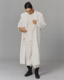 Imane Khelif wearing a white long coat and black boots against a neutral grey studio background for Mastermind Magazine.
