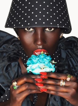 Close-up portrait of a Black model in a black and white polka dot hat eating a bright blue frosted cupcake