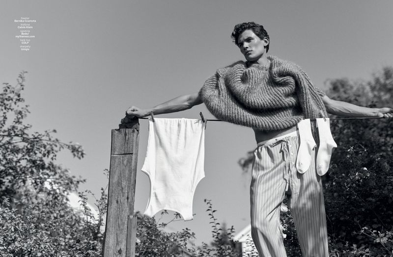 Monochrome fashion editorial image of a male model leaning on a washing line with garments hanging outdoors.