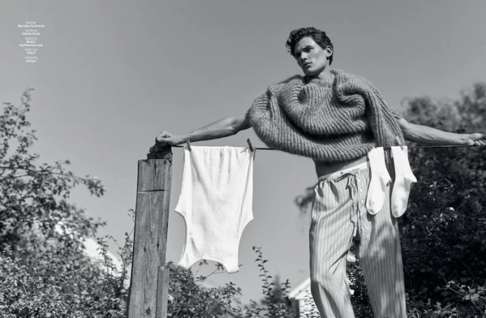 Monochrome fashion editorial image of a male model leaning on a washing line with garments hanging outdoors.