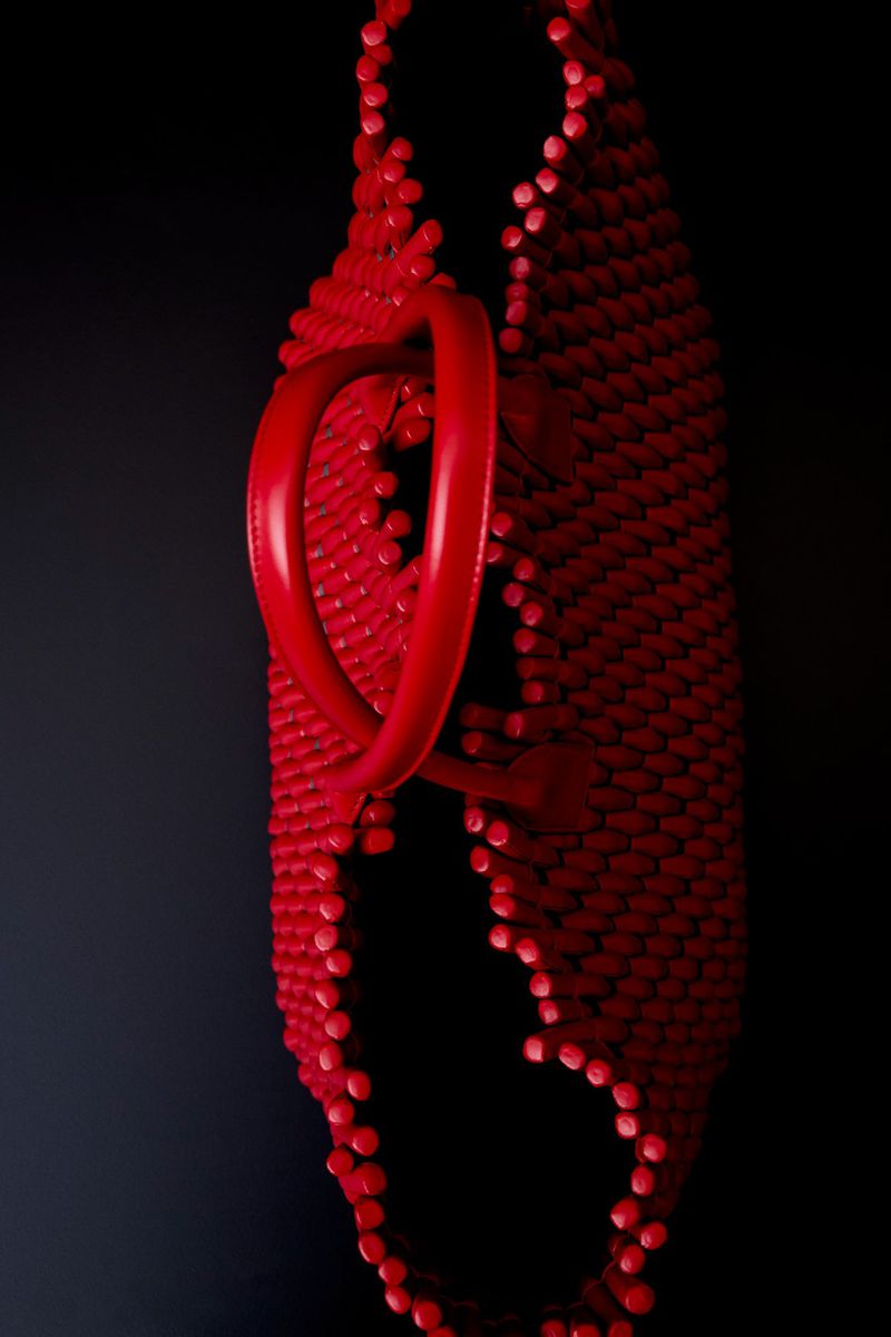 Close-up of a red textured sculptural handbag against a dark background for Bottega Veneta