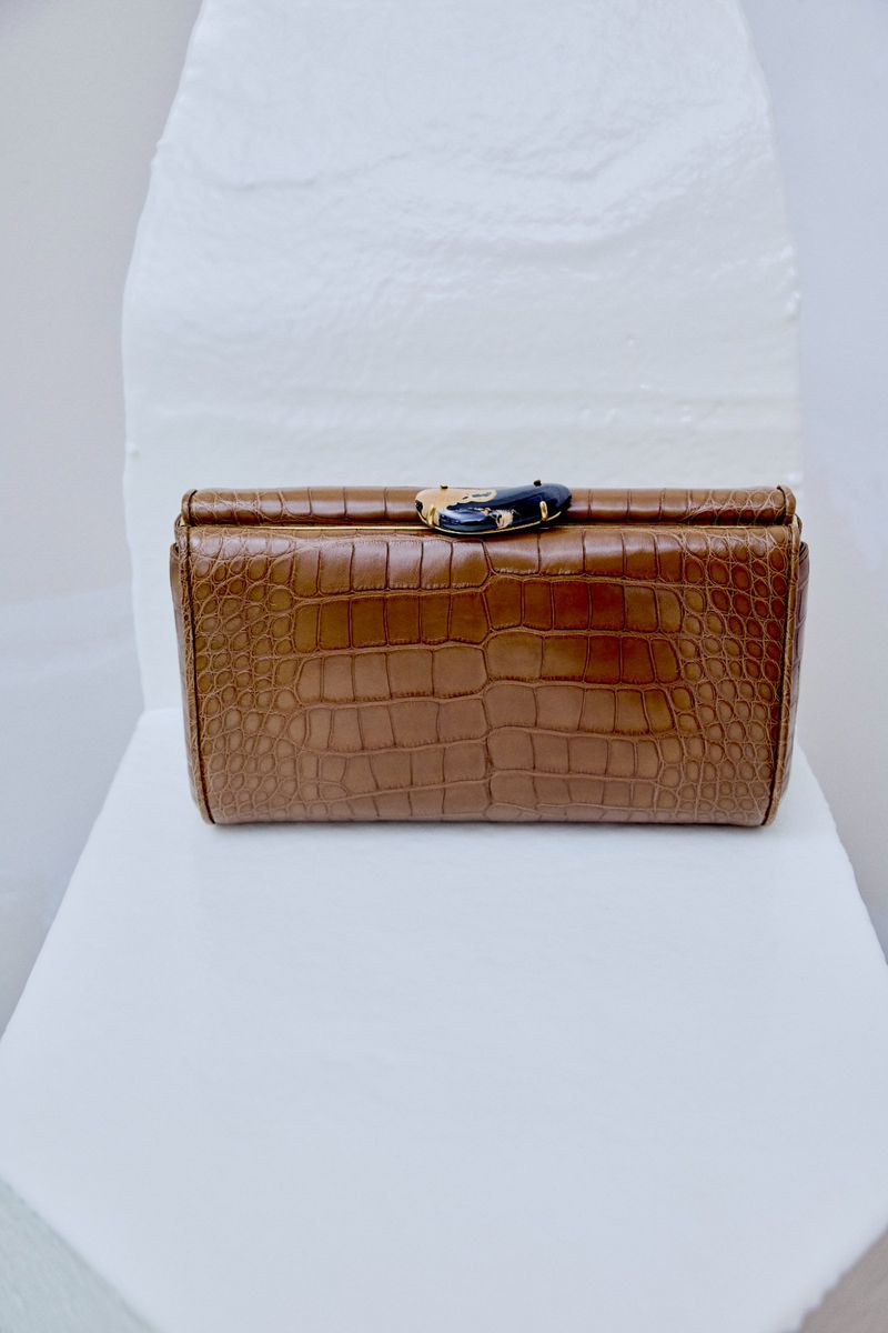 Brown embossed leather clutch bag with a decorative clasp resting on a sculptural white surface