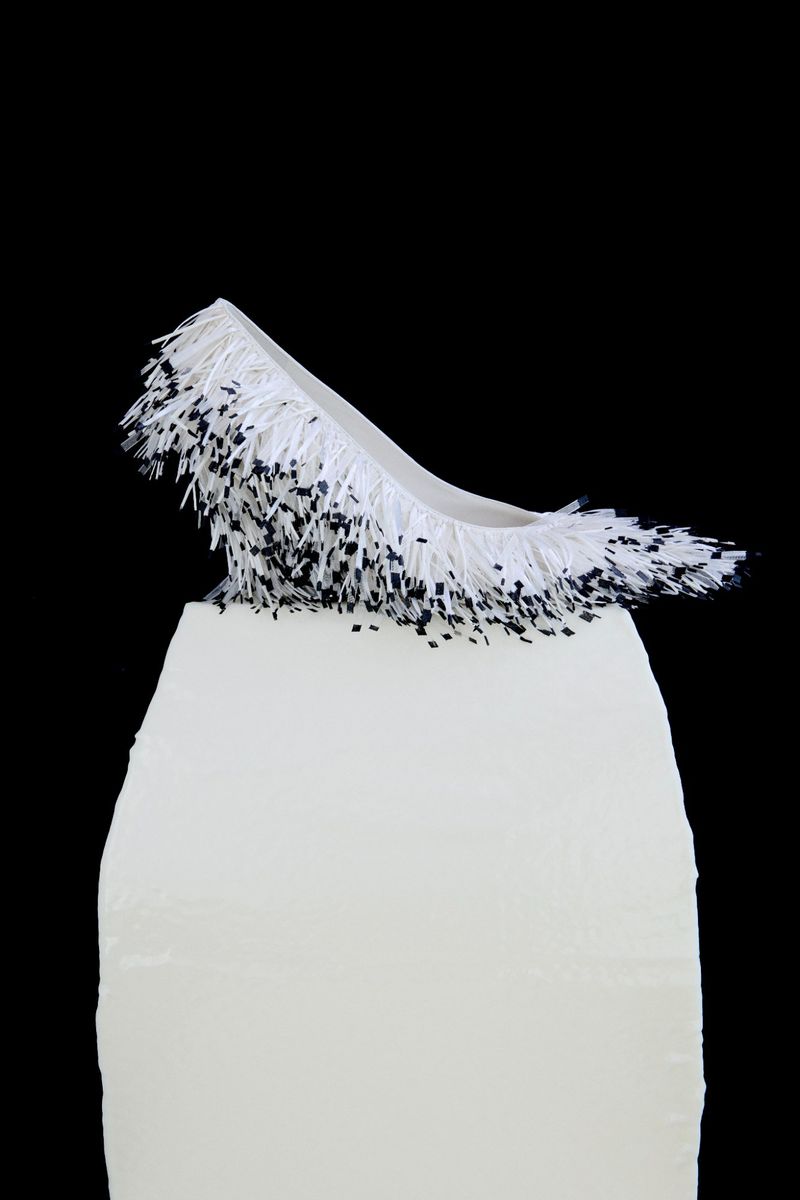 White fringe pump shoe resting on a white rectangular pedestal against a solid black background.