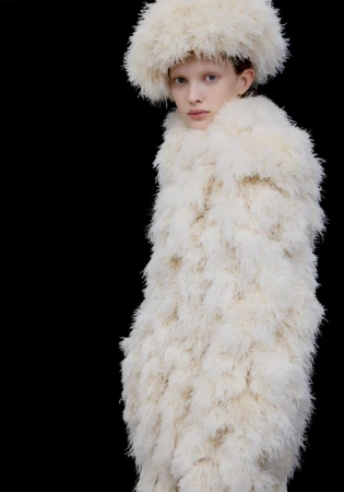 Model wearing a fluffy textured cream coat and matching hat against a plain black background.