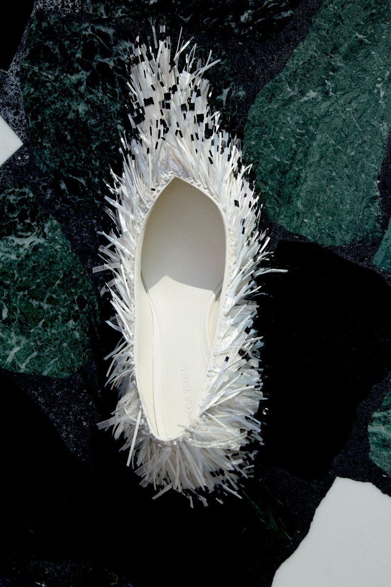 White fringed flat shoe on a dark green and black patterned marble surface