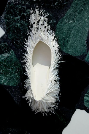 White fringed flat shoe on a dark green and black patterned marble surface