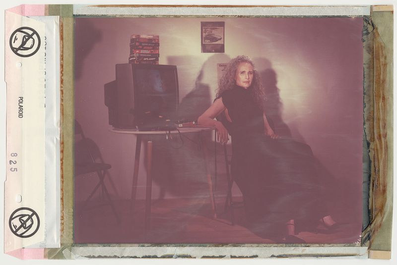 Andie MacDowell seated beside a small table and television in a vintage-toned portrait inside Crash Magazine.