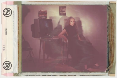 Andie MacDowell seated beside a small table and television in a vintage-toned portrait inside Crash Magazine.