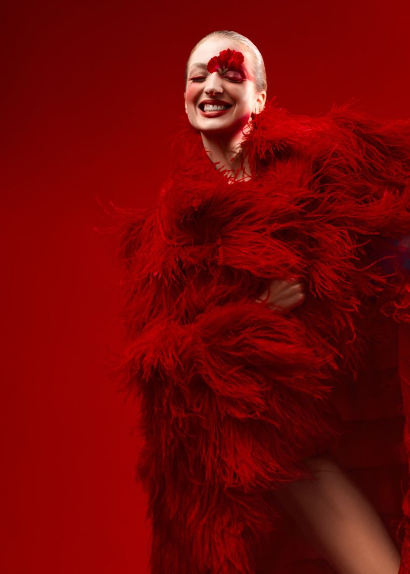 Smiling woman with red flower on her face wearing a red feathered coat in a studio. Beauty and fashion photography.