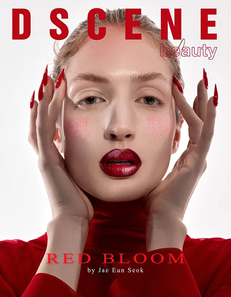 Close-up of an adult female model with red lipstick and long red nails against a light background, wearing a red turtleneck shirt.
