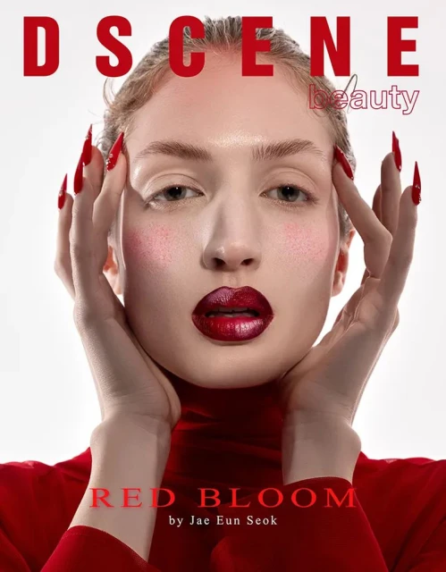 Close-up of an adult female model with red lipstick and long red nails against a light background, wearing a red turtleneck shirt.