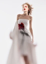 Model posing in a strapless white dress featuring a bold red floral print against a clean white studio backdrop.