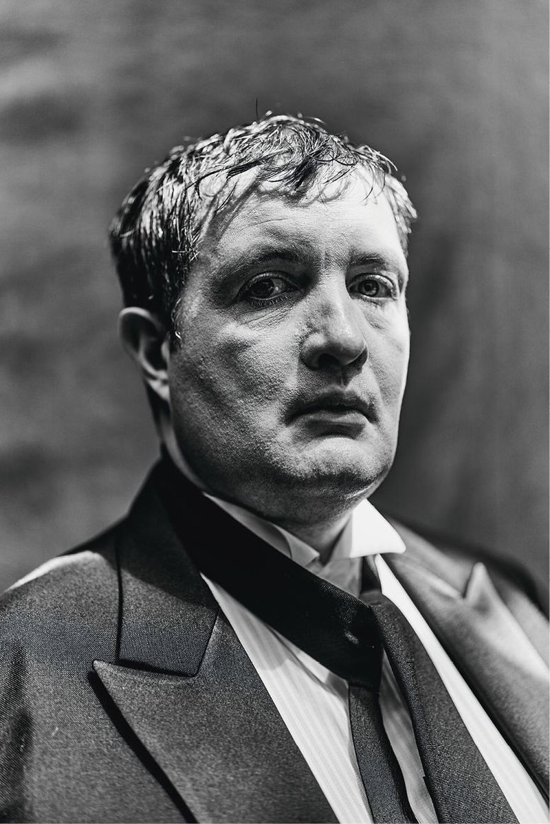 Portrait of a man in a dark suit and tie looking directly at the camera in a monochrome photograph.