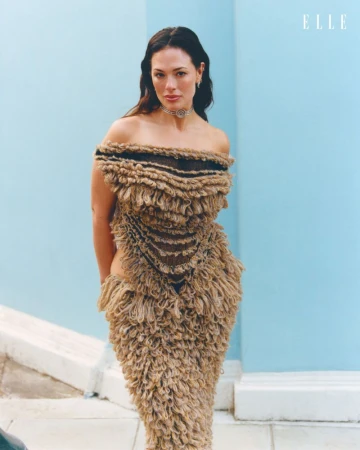 Ashley Graham wearing a textured shaggy brown strapless dress against a pale blue wall for Elle Netherlands.