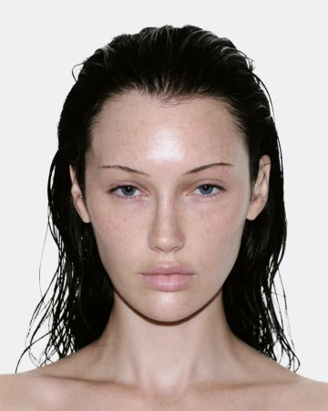 Close-up portrait of model Meredith Duxbury with wet dark hair and neutral expression against a white backdrop.