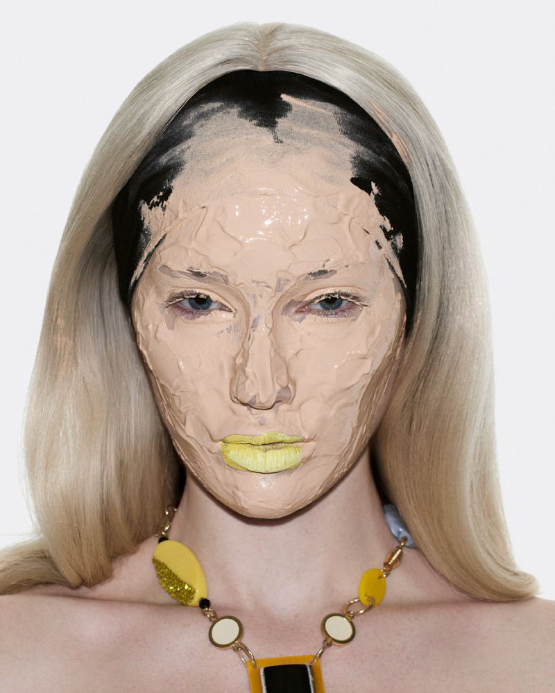 Close-up beauty portrait of Meredith Duxbury with thick layered foundation and yellow lipstick against a plain white background